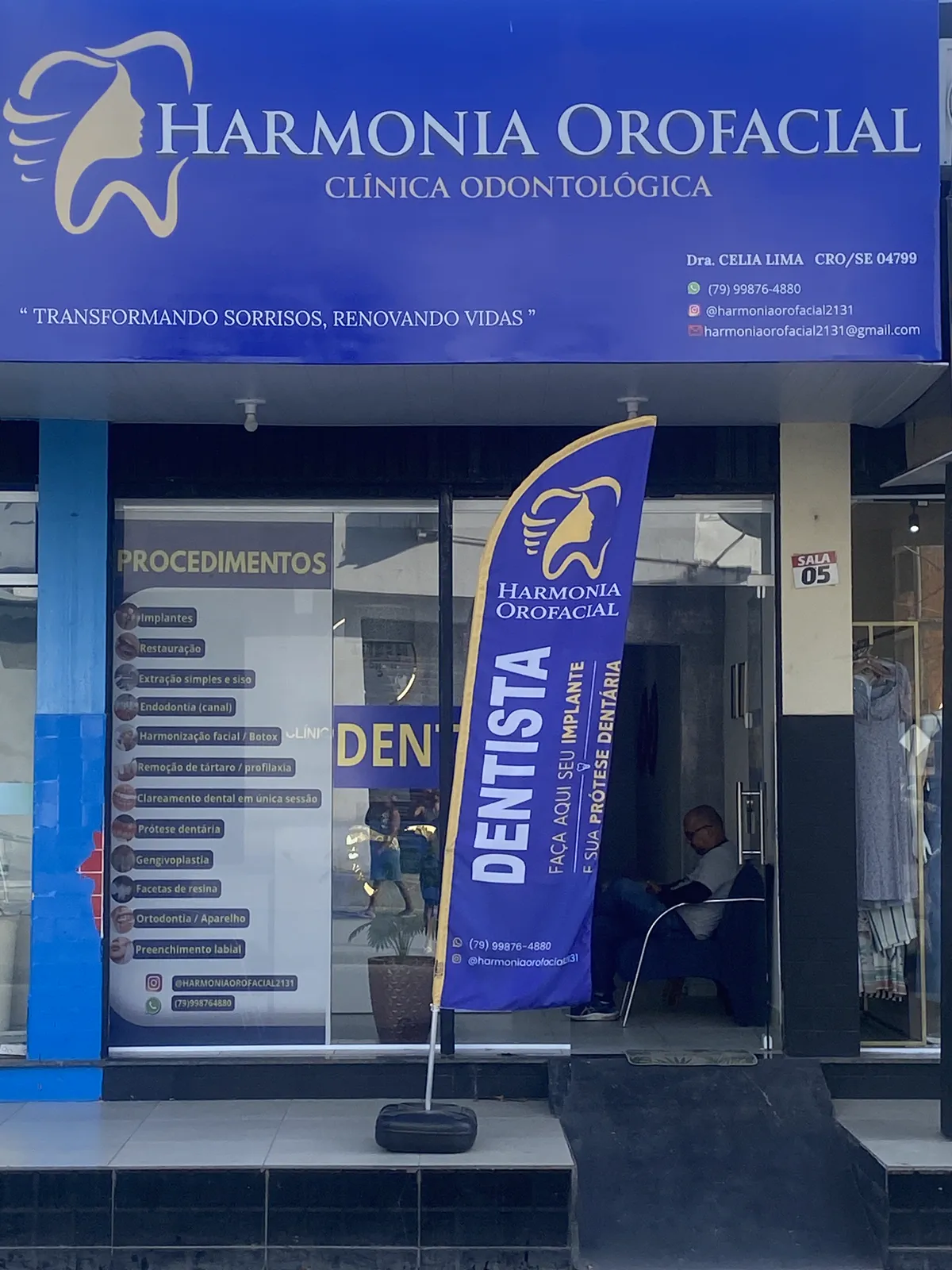Fachada da clínica, com o letreiro Harmonia Orofacial e a bandeira azul na calçada