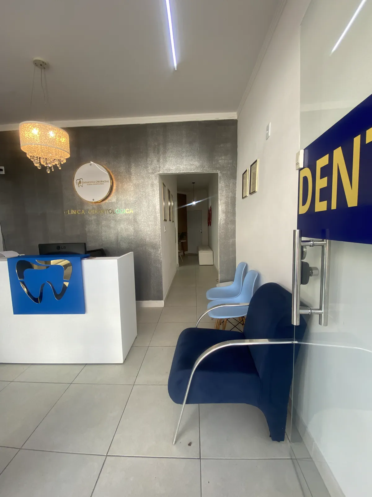 Sala de espera com cadeiras azuis e o corredor dos consultórios ao fundo